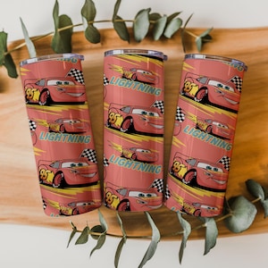 May include: Three red tumblers with a repeating pattern of the character Lightning McQueen from the movie Cars. The design includes the number 95, a checkered flag, and the word "LIGHTNING" in a yellow font. The tumblers are cylindrical and have a silver rim.