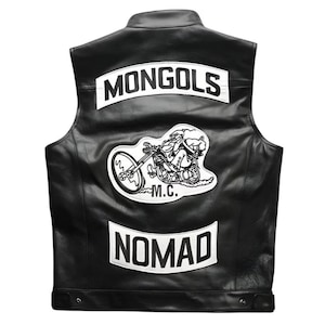 Könnte beinhalten: Schwarze Lederweste mit weißen Aufnähern. Der obere Aufnäher trägt die Aufschrift "MONGOLS" in weißen Blockbuchstaben. Ein zentraler Aufnäher zeigt ein Motorrad mit Fahrer, und der untere Aufnäher trägt die Aufschrift "NOMAD". Die Weste hat einen klassischen Biker-Stil.