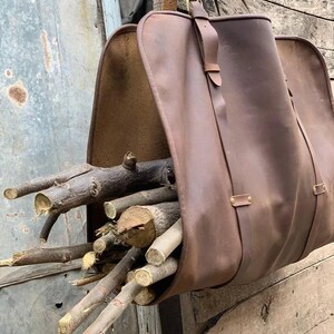 Può includere: Una borsa porta legna in pelle marrone piena di legna da ardere. La borsa ha una tracolla ed è appesa a un gancio di metallo. La borsa è realizzata in pelle robusta ed è progettata per trasportare i ceppi.