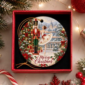 May include: A round ceramic Christmas ornament featuring a nutcracker soldier and a ballerina in a white tutu dancing in a snowy landscape with a castle. The text Merry Christmas is printed in red script at the bottom of the ornament.