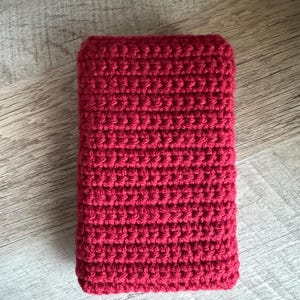 May include: A red crocheted rectangular pouch or case. The pouch is made with a simple stitch pattern and has a smooth, even texture.