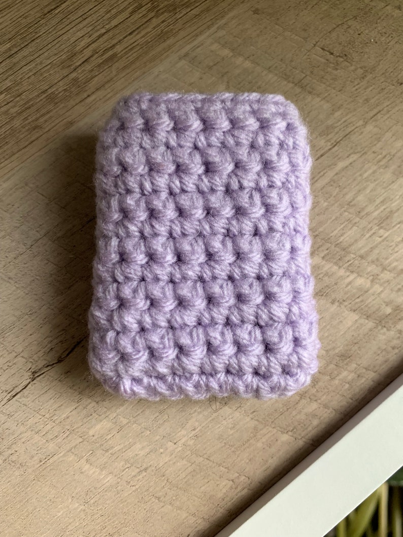 May include: A small, lavender crocheted pouch. The pouch is made with a single crochet stitch and has a smooth, textured surface.