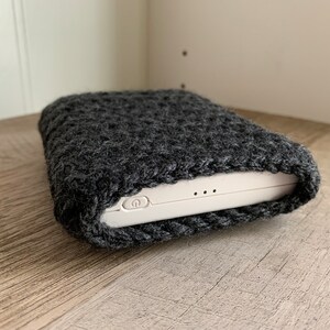 K&ouml;nnte beinhalten: Eine graue Strickh&uuml;lle f&uuml;r ein wei&szlig;es elektronisches Ger&auml;t. Die H&uuml;lle besteht aus einem weichen, flauschigen Material und hat einen Rei&szlig;verschluss. Das Ger&auml;t hat einen Ein- / Ausschalter und zwei kleine L&ouml;cher an der Seite.