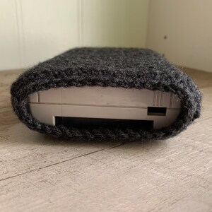 May include: A gray knitted case for a handheld gaming device. The case is made of a soft, fuzzy material and has a snug fit.