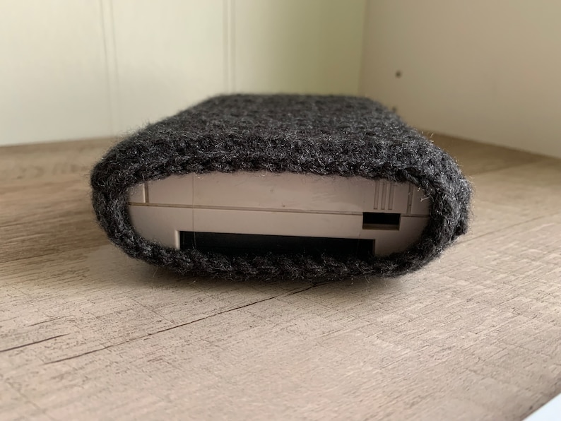 May include: A gray knitted case for a handheld gaming device. The case is made of a soft, fuzzy material and has a snug fit.