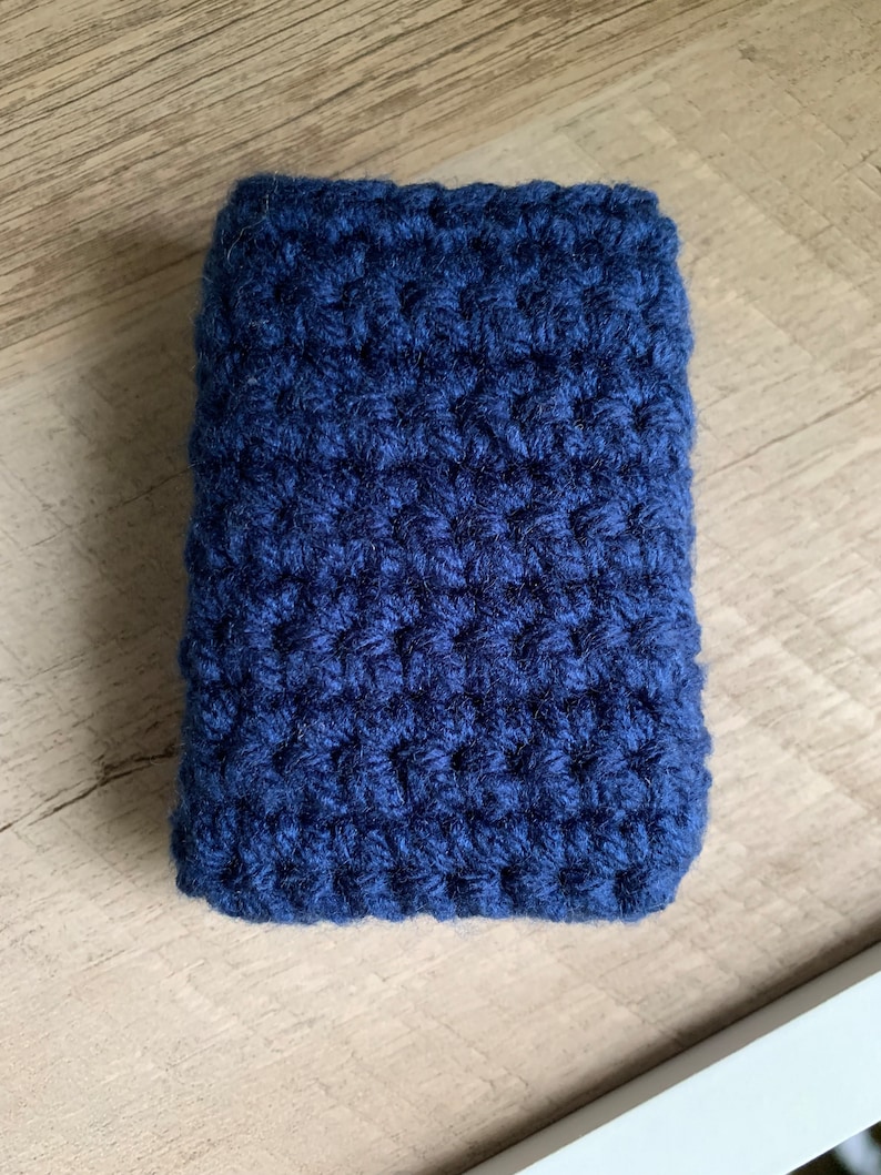 May include: A dark blue crocheted pouch or case. The pouch is made with a textured stitch and has a rectangular shape.