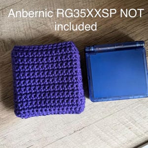 May include: A purple crocheted case and a blue handheld gaming device are displayed on a wooden surface. The case is rectangular and appears to be handmade. The text "Anbernic RG35XXSP NOT included" is visible.