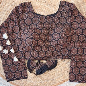 May include: A long-sleeved blouse with a dark navy blue background and a repeating floral pattern in shades of brown and tan. The blouse has a scoop neckline and a matching fabric accessory.