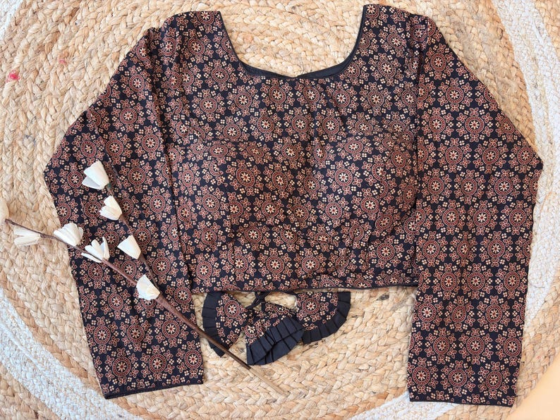 May include: A long-sleeved blouse with a dark navy blue background and a repeating floral pattern in shades of brown and tan. The blouse has a scoop neckline and a matching fabric accessory.