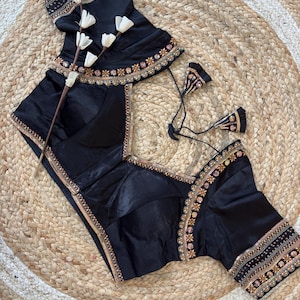 May include: Black silk blouse with intricate gold and pink embroidery along the neckline, sleeves, and hem. The blouse features a V-neck design and short sleeves. A matching black skirt is also visible.