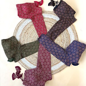 May include: An assortment of patterned blouses in various colors, including red, navy, and green, are arranged on a woven jute rug. Each blouse features a floral design and is displayed with matching accessories. The blouses are laid out on a neutral background.