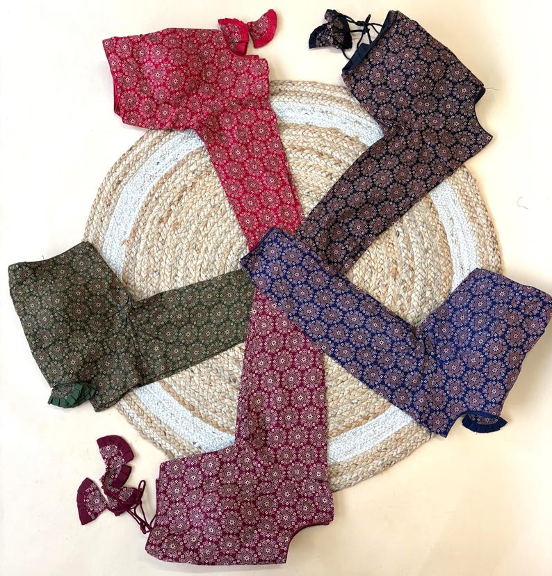 May include: An assortment of patterned blouses in various colors, including red, navy, and green, are arranged on a woven jute rug. Each blouse features a floral design and is displayed with matching accessories. The blouses are laid out on a neutral background.