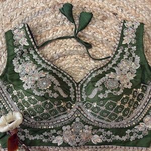 Puede incluir: Una blusa sin mangas de color verde oliva con intrincados bordados y lentejuelas. El corpiño presenta un escote en V profundo y un patrón decorativo. La blusa tiene un cierre de lazo en la parte posterior del cuello. Es probable que sea una blusa o un top corto.