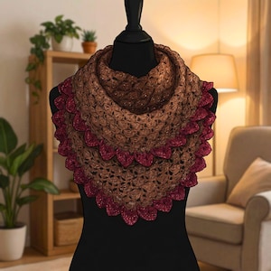 May include: A brown and burgundy crochet shawl displayed on a black mannequin. The shawl features a textured pattern with a scalloped burgundy border. The color palette includes shades of brown and burgundy, creating a warm and inviting aesthetic. The shawl is a handmade accessory.