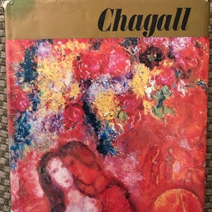 May include: A book cover featuring the name "Chagall" in black lettering above a vibrant painting. The artwork depicts a couple embracing amidst a colorful floral background dominated by red and yellow hues.