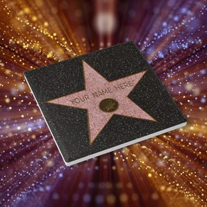 May include: A pink star with the text "YOUR NAME HERE" on a black background. The star is surrounded by a black border and has a small, silver film camera icon in the centre.