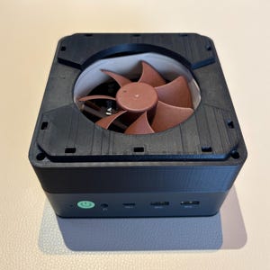 Puede incluir: Una carcasa de ordenador negra con un ventilador de color cobre visible en el interior. La carcasa tiene un botón de encendido y varios puertos USB en la parte delantera. El ventilador tiene múltiples aspas y está centrado en la carcasa.