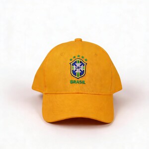 May include: A yellow baseball cap with the Brazilian Football Confederation (CBF) emblem. The emblem features a shield with a cross, stars, and the word "BRASIL" in green. The cap is made of a soft material.