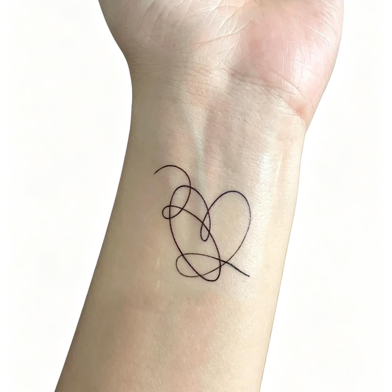 May include: A black line art tattoo of a heart shape on a wrist. The heart is formed by a continuous, looping line. The skin tone is light, and the background is plain white.