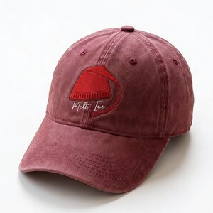 Può includere: Cappellino da baseball bordeaux con visiera curva. Il cappellino presenta un ricamo rosso con un design a fez e le parole "Melt Ice" in corsivo bianco. Il cappellino è realizzato in un tessuto morbido e strutturato.