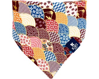 Op de afbeelding: Een kleurrijke bandana voor honden met een Japans geïnspireerd ontwerp. De bandana heeft een herhalend patroon van waaiervormige motieven in rood, blauw, geel en wit. Een klein blauw label met witte tekst is bevestigd.