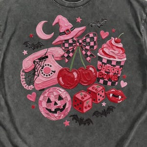 May include: A charcoal gray short-sleeve t-shirt featuring a graphic print of a pink rotary phone, a witch hat, a disco ball pumpkin, red dice, cherries, and a cup labeled Cherry Bomb. The design includes small bats, stars, and hearts.