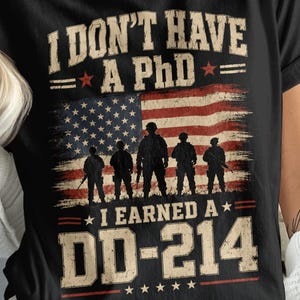 May include: A black short-sleeve t-shirt featuring a graphic with the text I DON'T HAVE A PhD I EARNED A DD-214. The design includes a distressed American flag background with silhouettes of five soldiers standing in front of the flag stripes.