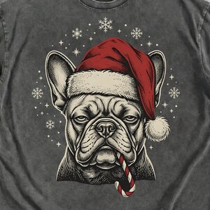 Peut inclure: Un t-shirt gris anthracite orné d'une illustration graphique d'un bouledogue français portant un bonnet de Père Noël rouge et tenant un sucre d'orge dans sa gueule, entouré d'un motif circulaire de flocons de neige blancs.