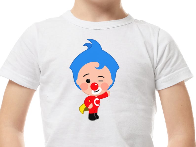 May include: White t-shirt featuring a cartoon character with blue hair, a red nose, and a red outfit with a yellow cape. The character is winking and has a smiling expression. The shirt is made of a soft, comfortable material.