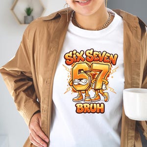 May include: White t-shirt featuring a cartoon graphic with the text "SIX SEVEN BRUH". The numbers 6 and 7 are anthropomorphic characters in orange and yellow, with lightning bolts. The shirt is worn by a person.