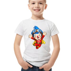 Puede incluir: Camiseta blanca de manga corta con un personaje de dibujos animados con un atuendo de piloto. El personaje tiene pelo azul, gafas, un traje rojo y una capa amarilla. El dise&ntilde;o est&aacute; centrado.