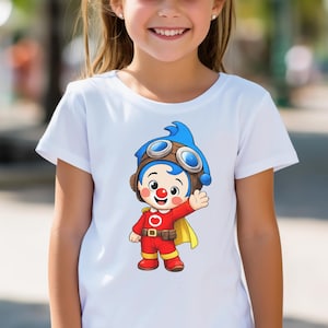 Puede incluir: Camiseta blanca con un personaje de dibujos animados. El personaje tiene pelo azul, gafas y un traje rojo. El personaje est&aacute; saludando. La camiseta es de cuello redondo.