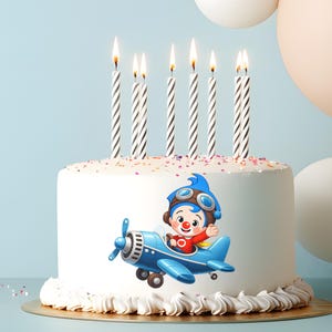 Puede incluir: Una tarta de cumplea&ntilde;os blanca decorada con un piloto de dibujos animados en un avi&oacute;n azul. La tarta tiene siete velas a rayas encendidas y est&aacute; sobre una base dorada. Hay confeti y globos en el fondo.