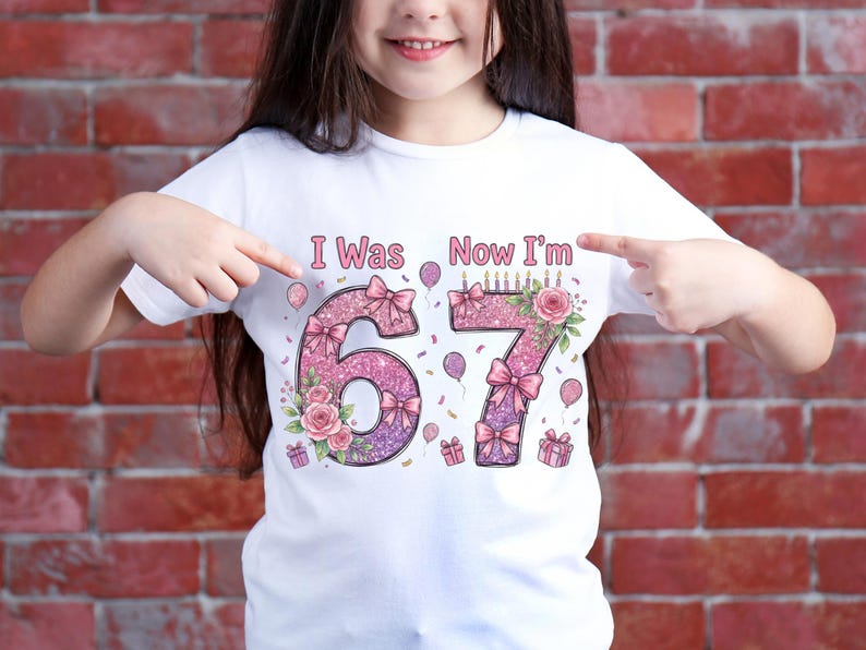 May include: White t-shirt with the text "I Was Now I'm" above the numbers 67. The numbers are decorated with pink glitter, bows, flowers, and birthday candles. Balloons and gift boxes are also featured.