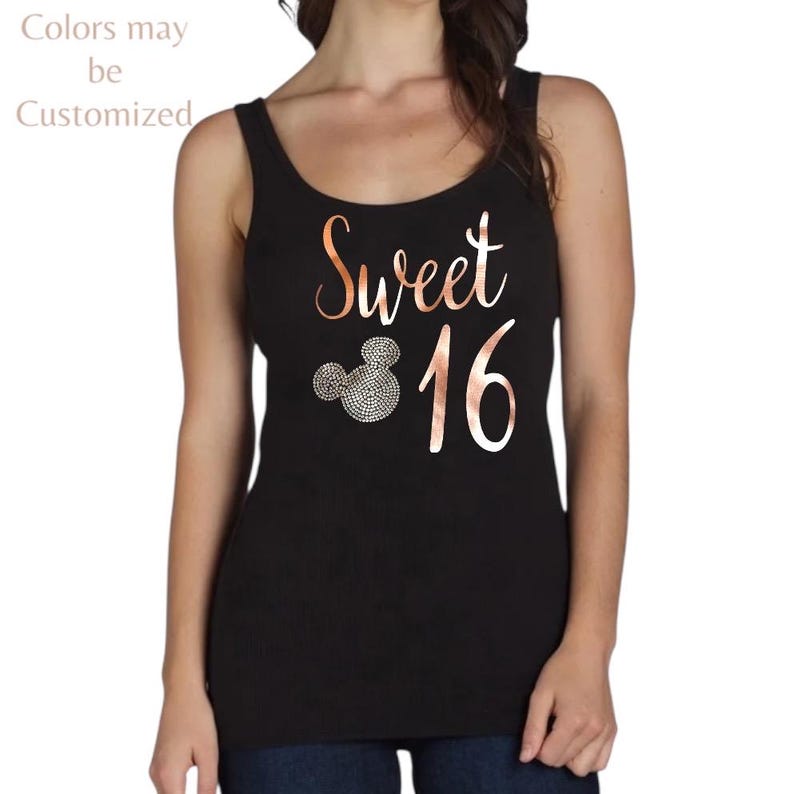 May include: A black tank top featuring the rose gold text Sweet 16 and a circular icon resembling a mouse head filled with small silver rhinestones. The text Colors may be Customized is printed in the upper left corner of the image.