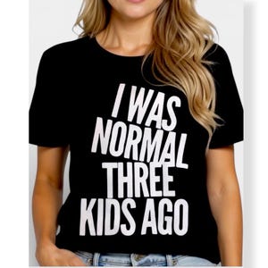 May include: Black t-shirt with the white text "I WAS NORMAL THREE KIDS AGO". The shirt has short sleeves and a crew neck. The image shows the shirt on a person.