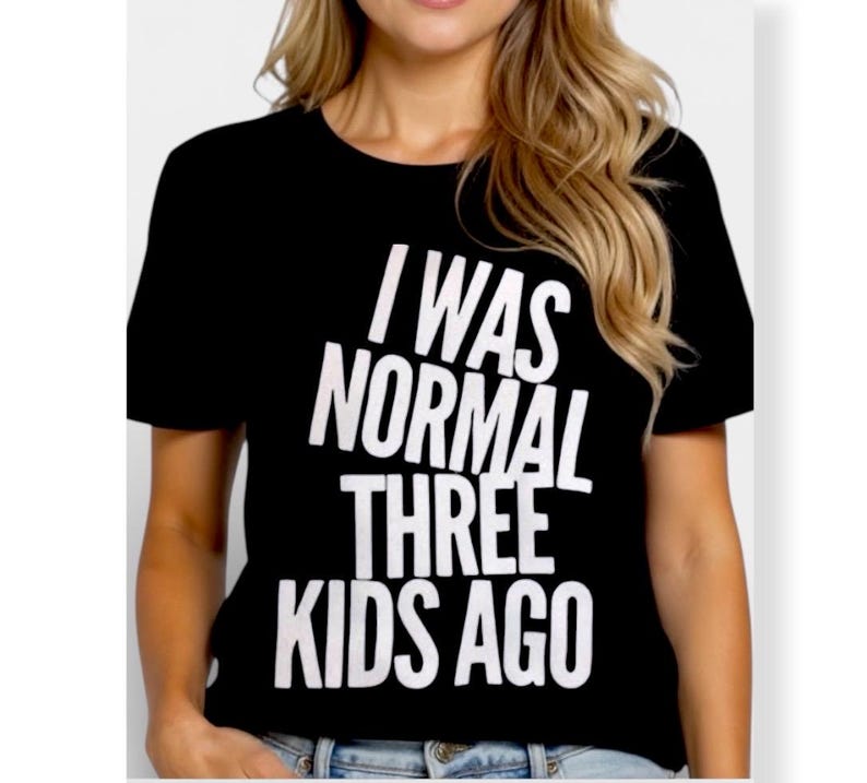 May include: Black t-shirt with the white text "I WAS NORMAL THREE KIDS AGO". The shirt has short sleeves and a crew neck. The image shows the shirt on a person.