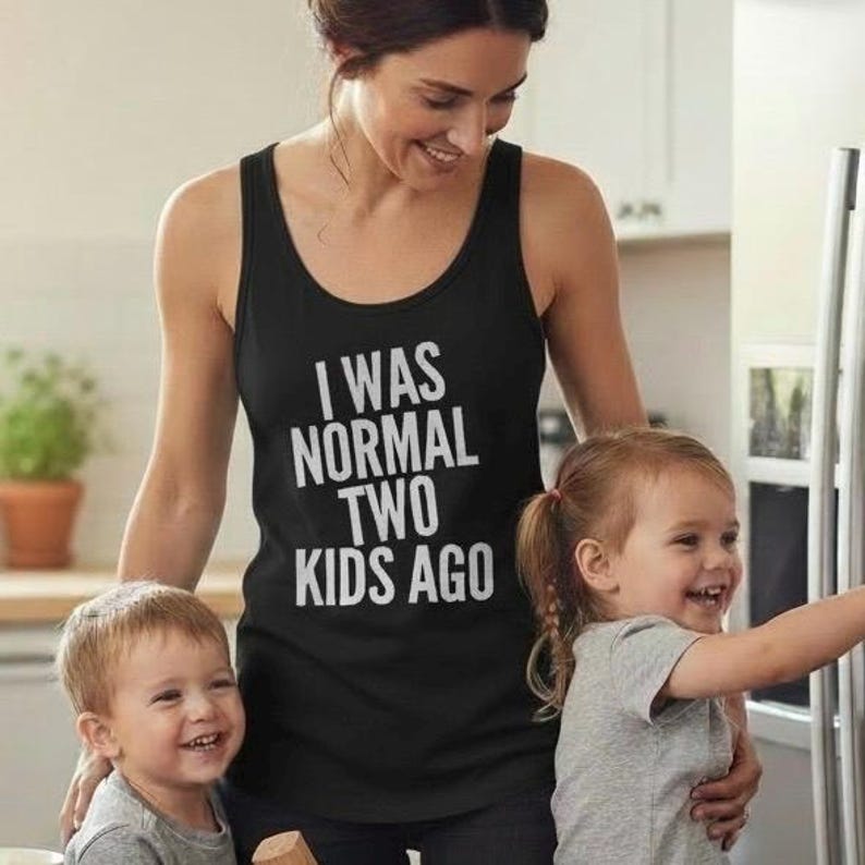 May include: Black tank top with the text "I WAS NORMAL TWO KIDS AGO" in white. The tank top is worn by a person standing with two young children. The children are smiling.