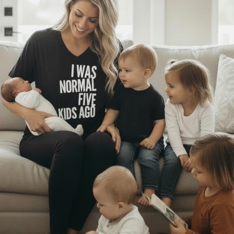 May include: A woman wearing a black v-neck shirt with the text "I WAS NORMAL FIVE KIDS AGO" sits on a couch with five children. The children are of various ages, including a newborn baby.