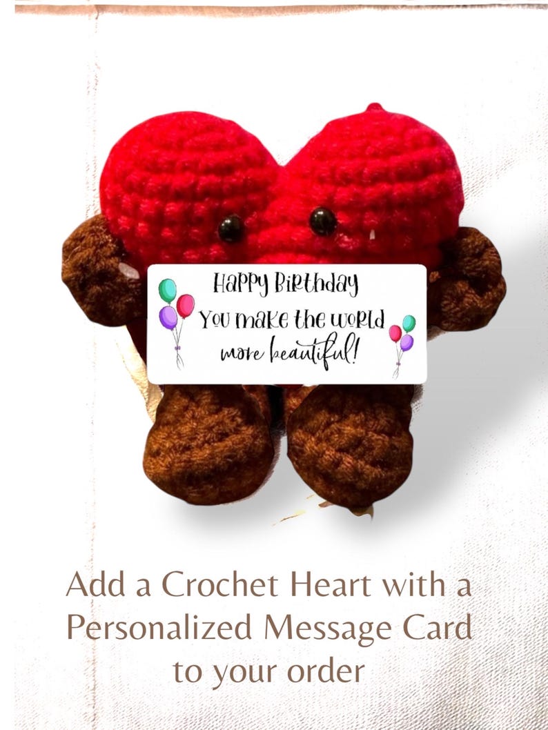 May include: A red crochet heart with brown arms and legs, featuring two black bead eyes. A white rectangular card is attached to the front with the text: Happy Birthday You make the world more beautiful! along with illustrations of colorful balloons.