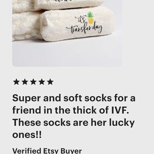 May include: White, fluffy socks with the phrases "WAKE & PRAY" and "it's transfer day" printed in black script. A pineapple graphic accompanies the second phrase. These socks are a thoughtful gift.