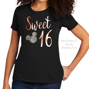 May include: A black short-sleeved t-shirt featuring the rose gold text Sweet 16. The design includes a mouse-ear silhouette filled with small silver-toned circular accents. The text The Perfect T for the Birthday Girl is printed on the right side.