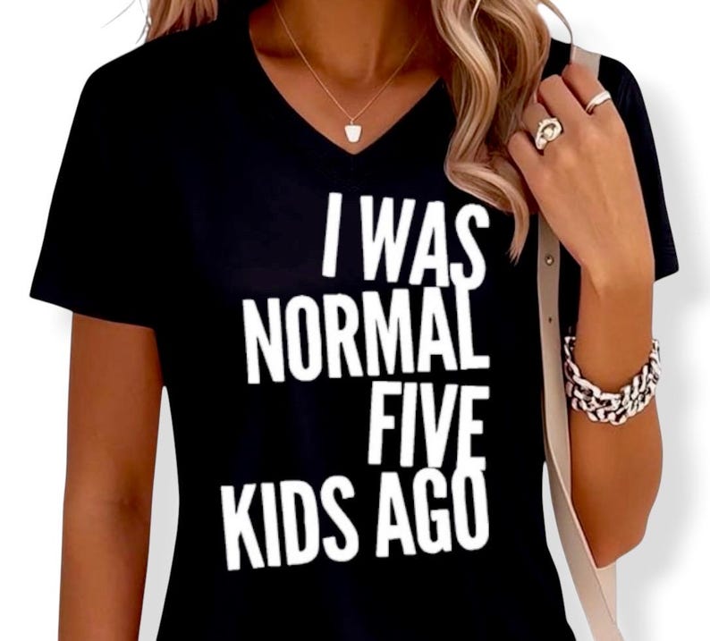May include: Black V-neck t-shirt with the white text "I WAS NORMAL FIVE KIDS AGO". The shirt is a short-sleeved top, suitable for casual wear. The text is in a bold, sans-serif font.