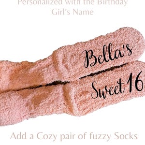 May include: A pair of light pink fuzzy socks featuring the black script text Bella's Sweet 16 printed on the fabric. The socks have a soft, textured appearance and are displayed against a plain white background with additional text.