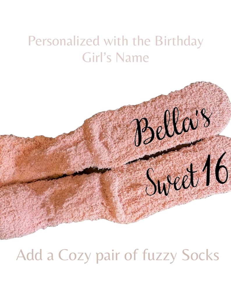 May include: A pair of light pink fuzzy socks featuring the black script text Bella's Sweet 16 printed on the fabric. The socks have a soft, textured appearance and are displayed against a plain white background with additional text.