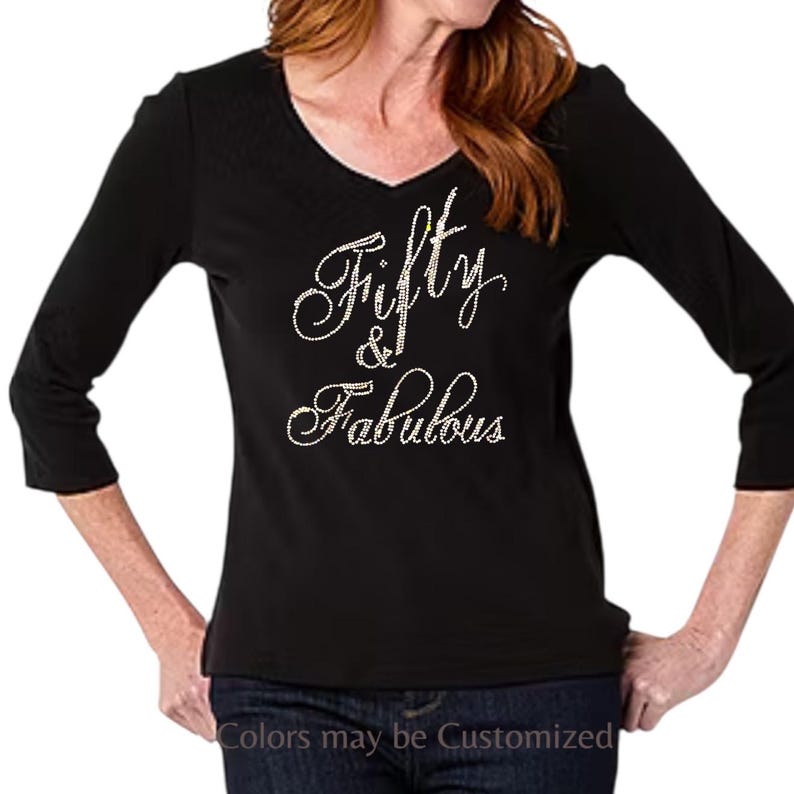 May include: Black V-neck shirt with three-quarter sleeves. The words "Fifty & Fabulous" are written in a cursive font with rhinestone embellishments. The text "Colors may be Customized" is at the bottom.