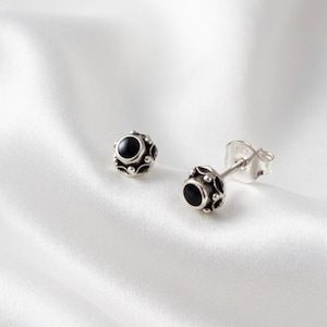 May include: A pair of sterling silver stud earrings featuring a round, polished black stone set in a decorative, scalloped metal frame. The back of the earring post is clearly stamped with the number 925, indicating the silver purity level.
