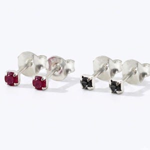 May include: Two pairs of stud earrings with silver-toned posts and backs. One pair features round, faceted deep red stones, while the other pair features round, faceted black stones. Each earring is secured with a standard friction post and backing.