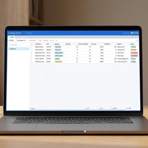 May include: A laptop displaying a spreadsheet on a wooden desk, with a white mug and a potted succulent. The laptop screen shows data in a table format. The scene is lit by natural light from a nearby window.