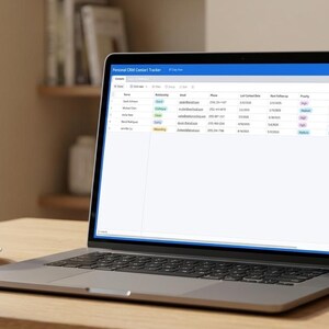 May include: A laptop displaying a spreadsheet on a wooden desk, with a white coffee cup and a small potted succulent. The laptop screen has a blue header and a grid of data. The scene is lit by natural light.